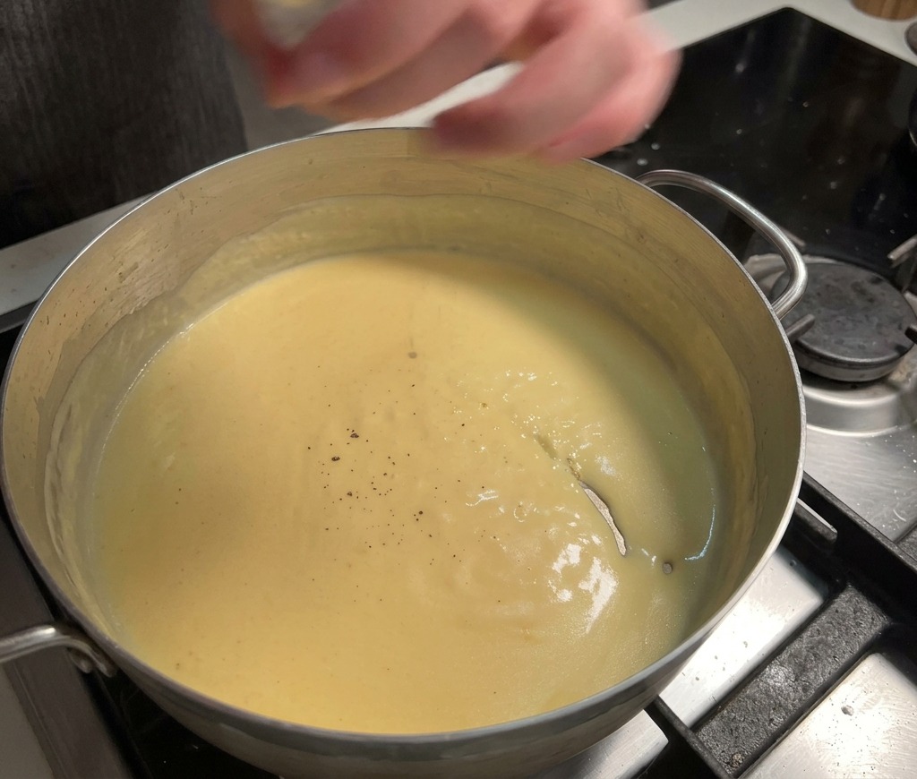 Poivre noir frais moulu dans une sauce au fromage jaune, épaisse et crémeuse, qui mijote dans une casserole.