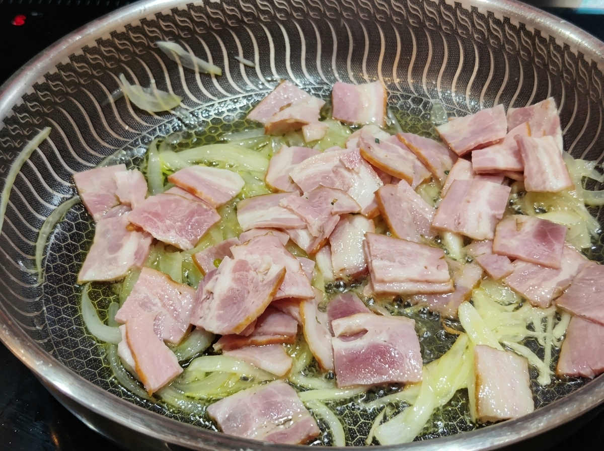 Morceaux de lardons roses cuisant dans une poêle aux côtés de lamelles doignons translucides.