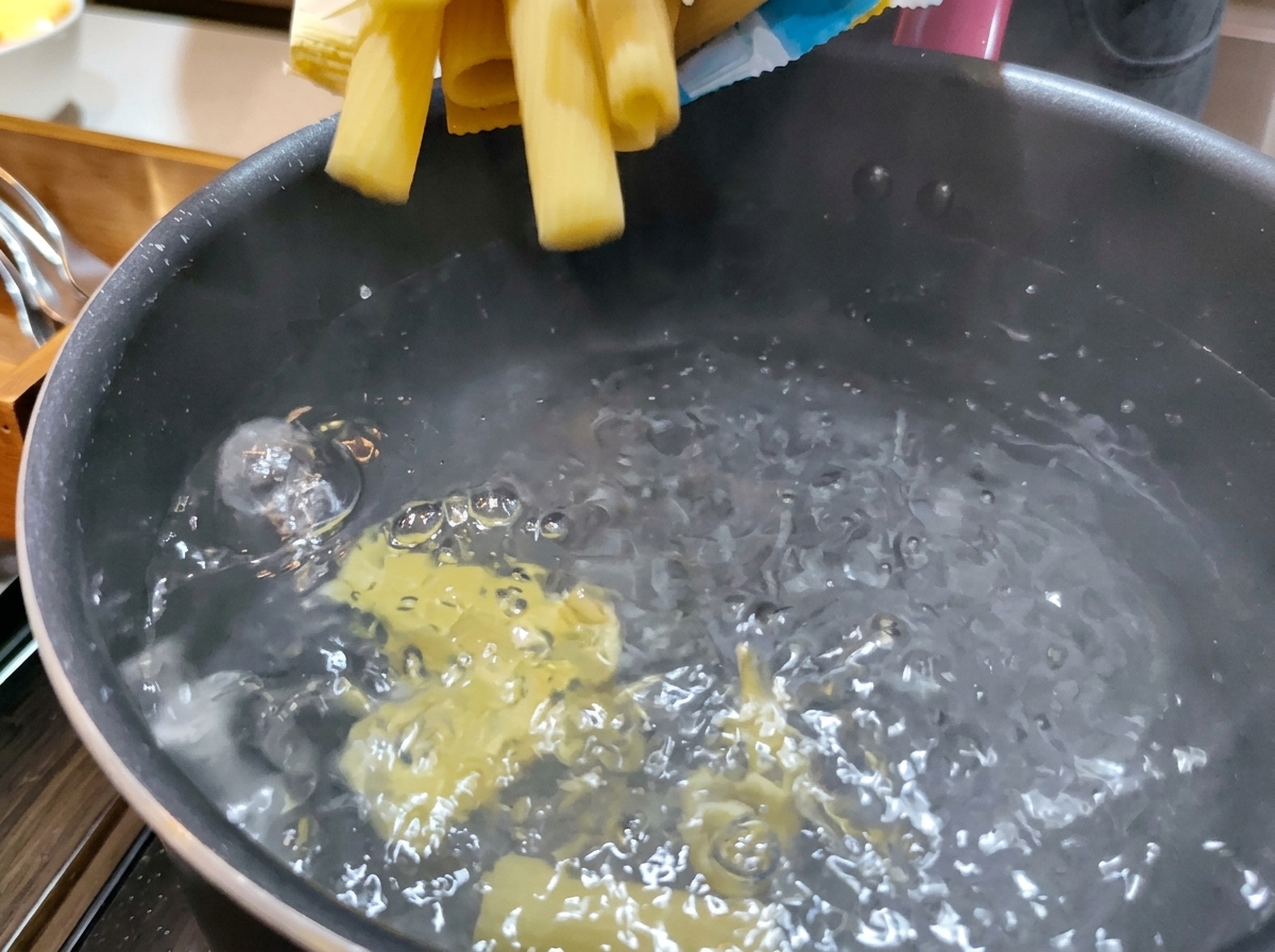 Pâtes rigatoni sèches et jaunes plongées dans une casserole deau bouillante et fumante.