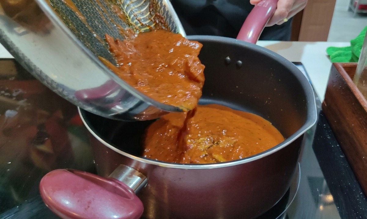 Sauce Amatriciana rouge chaude versée depuis une poêle dans une casserole de rigatoni égouttés.