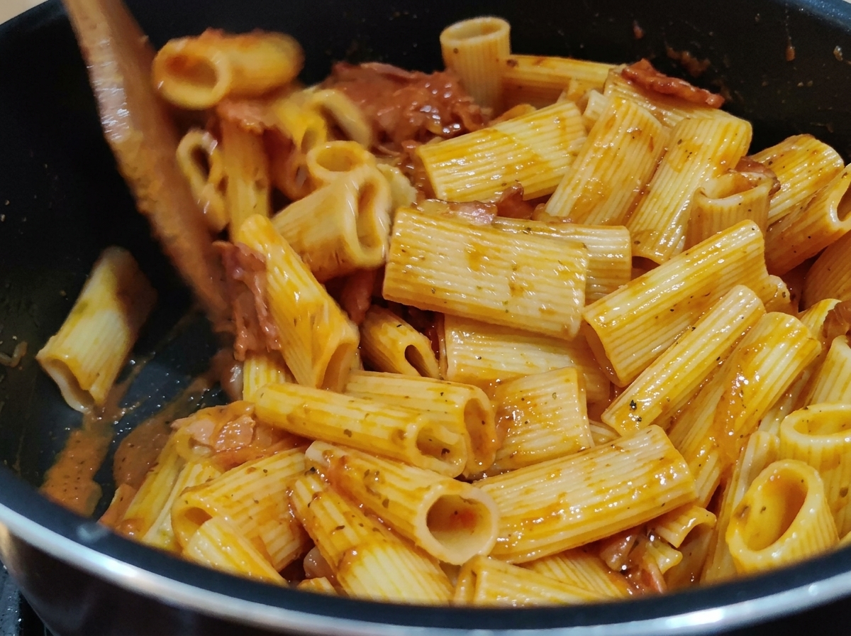 Mélange des rigatoni avec la riche sauce tomate rouge dans une casserole à laide dune spatule en bois.