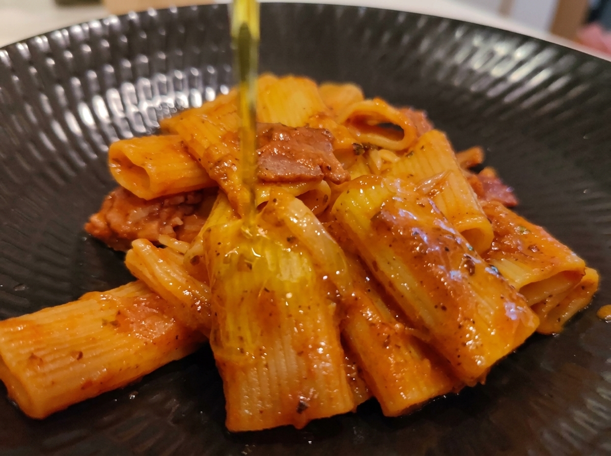 Un filet dhuile dolive extra-vierge versé sur une portion dressée de rigatoni à lamatriciana.