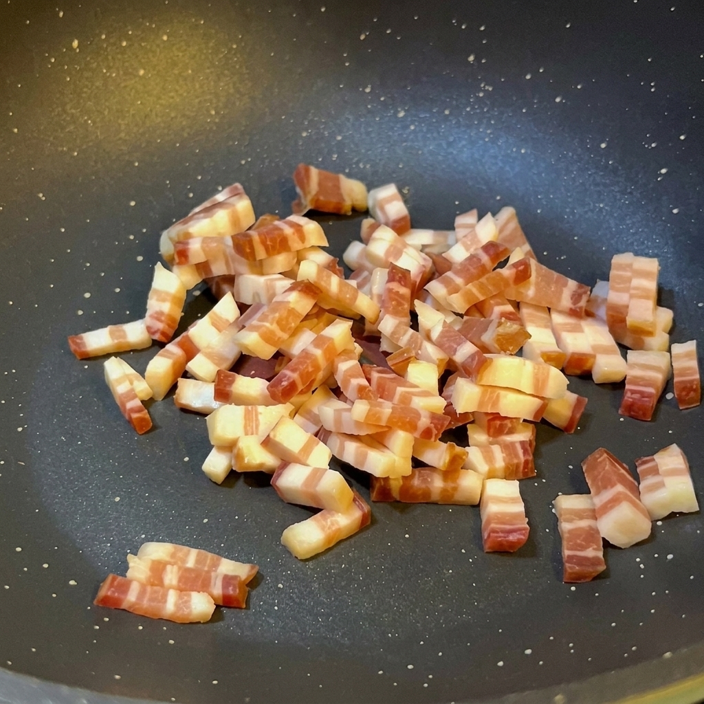 Petits dés de pancetta italienne sautant dans une poêle antiadhésive sombre, laissant apparaître du gras fondu et une légère coloration sur les bords.