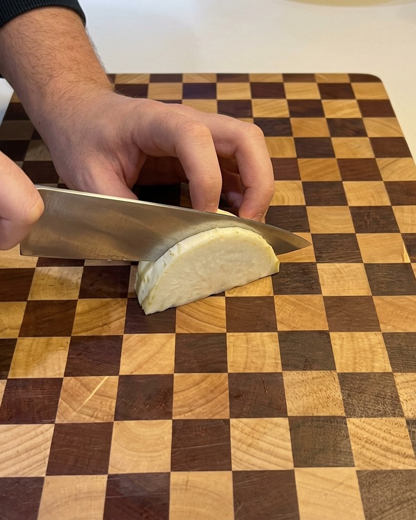 Une personne utilisant un couteau de chef pour émincer un quartier doignon blanc sur une planche à découper en bois.