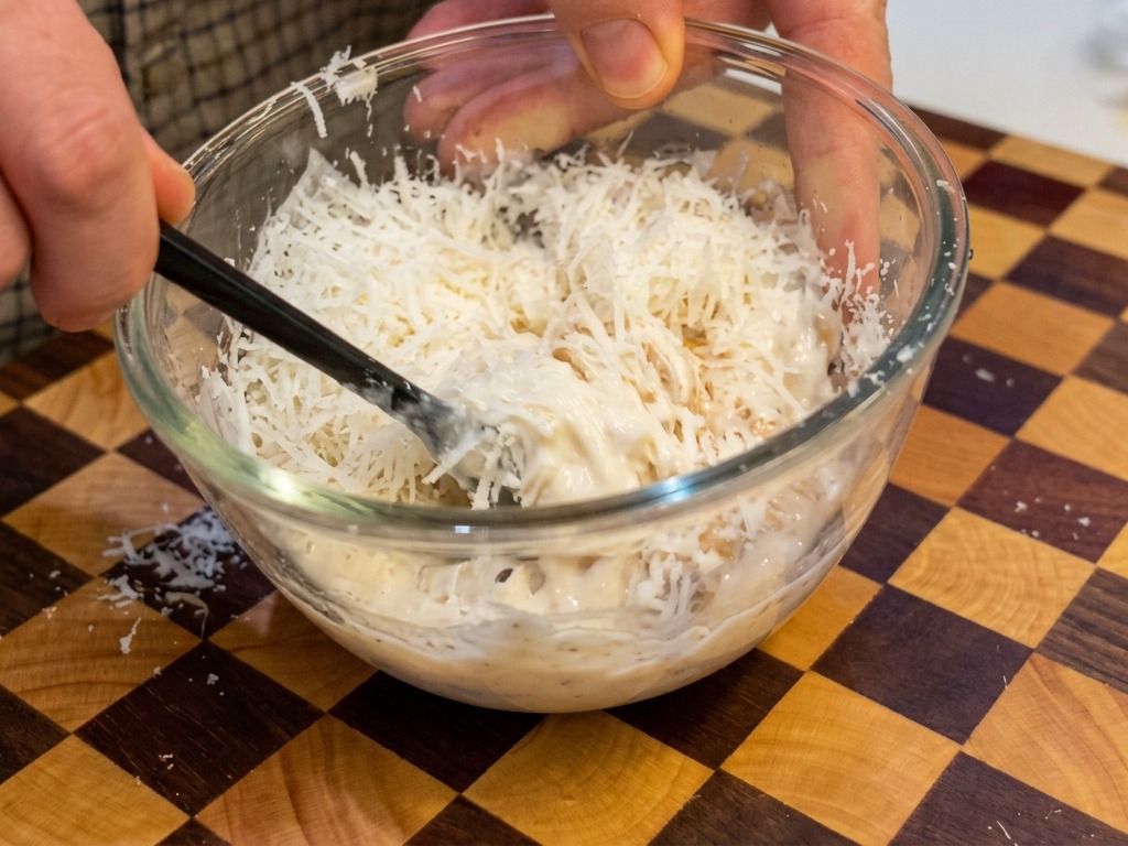Un mélange épais et crémeux jaune clair dœufs et de fromage remué avec des baguettes noires dans un bol transparent.