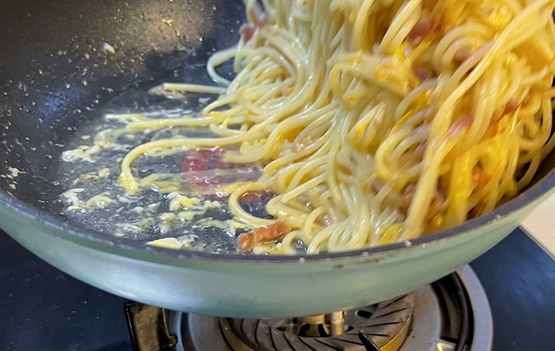 Une part magnifiquement dressée de spaghetti carbonara sur une assiette blanche en céramique, parsemée de fromage râpé et de poivre.