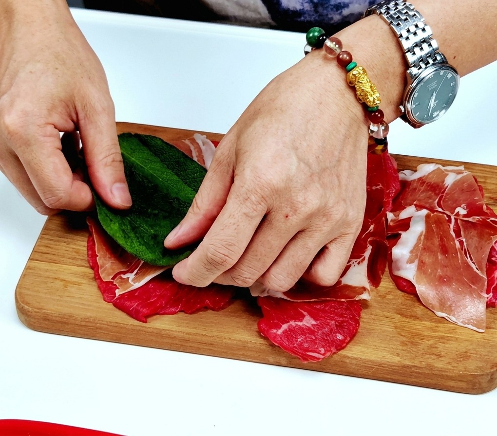 Mains plaçant une feuille de sauge fraîche sur le prosciutto.