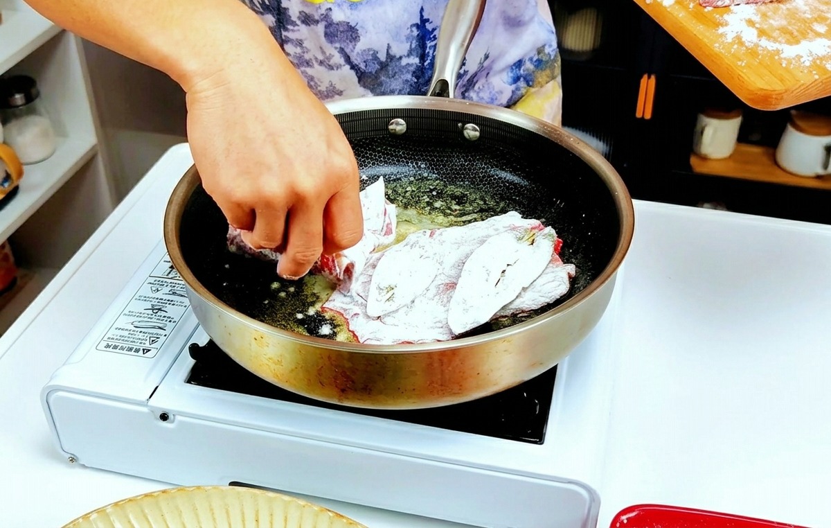 Mains déposant les escalopes de veau farinées dans la poêle chaude.