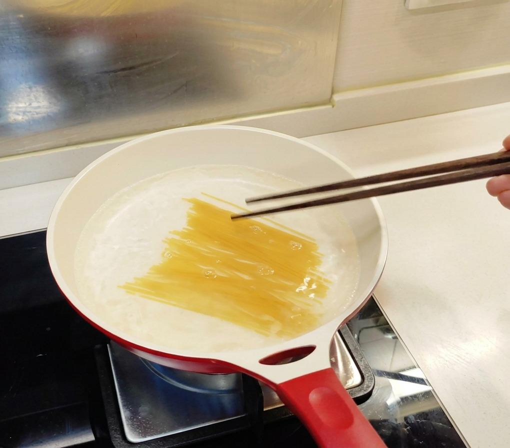 Spaghettis secs plongés dans une casserole deau bouillante à laide de baguettes en bois.