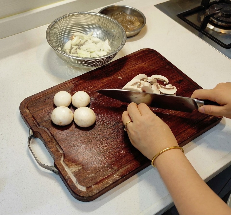 Une personne coupant des champignons de Paris en fines lamelles sur une planche en bois.