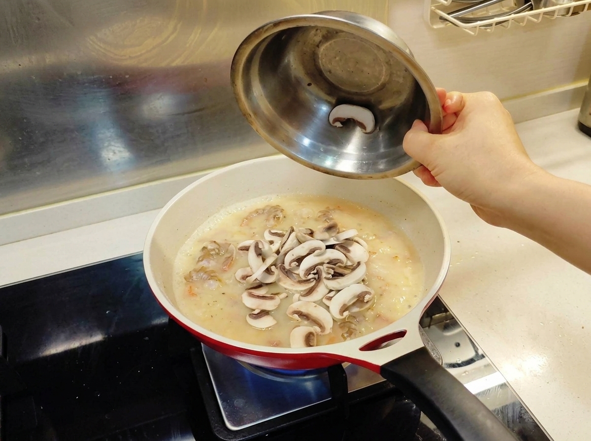 Lamelles de champignons frais versées depuis un bol en métal dans une poêle contenant les crevettes et la base de sauce.