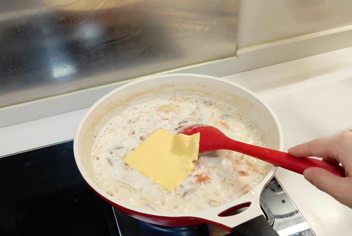 Une tranche carrée de fromage allégé déposée sur les pâtes en sauce blanche dans une poêle.