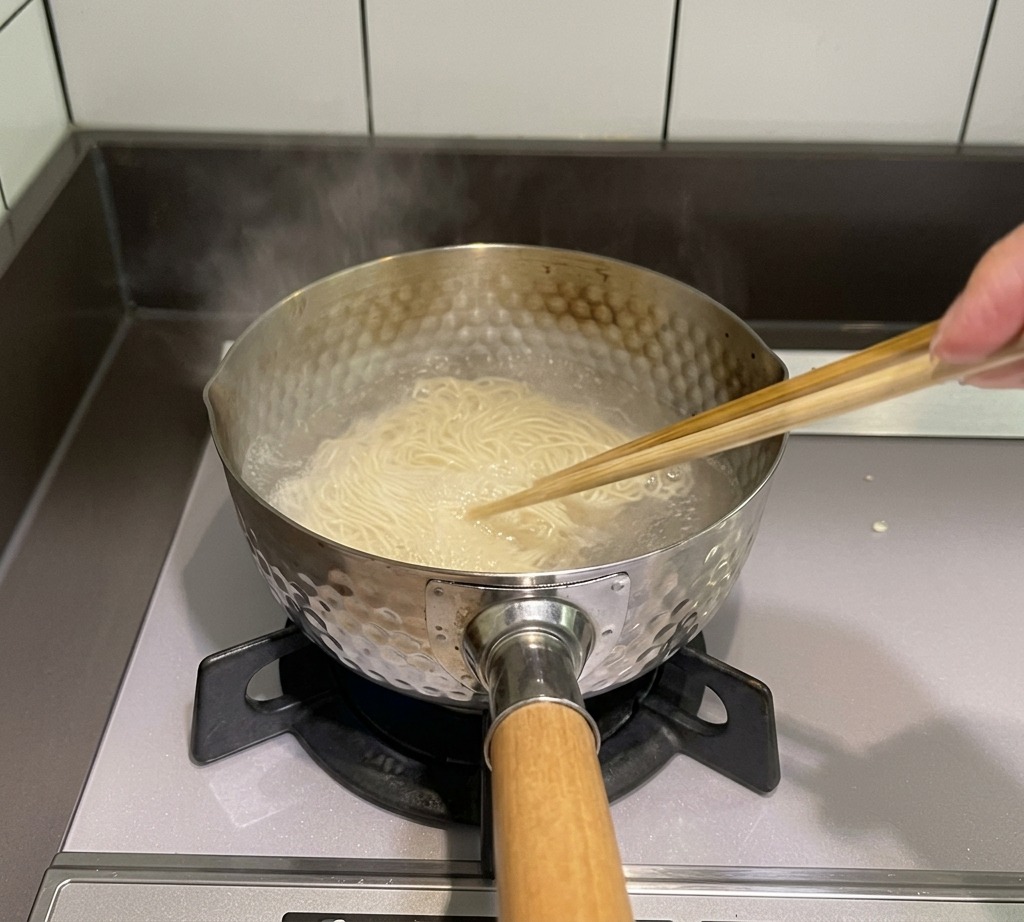 Une paire de baguettes en bois remue de fines nouilles dans une casserole deau bouillante sur le feu.