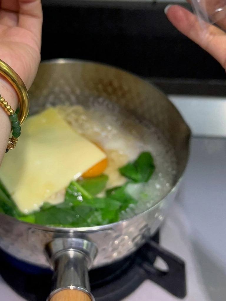Des tranches de fromage fondu jaune sont disposées sur un œuf et des nouilles dans une casserole fumante.