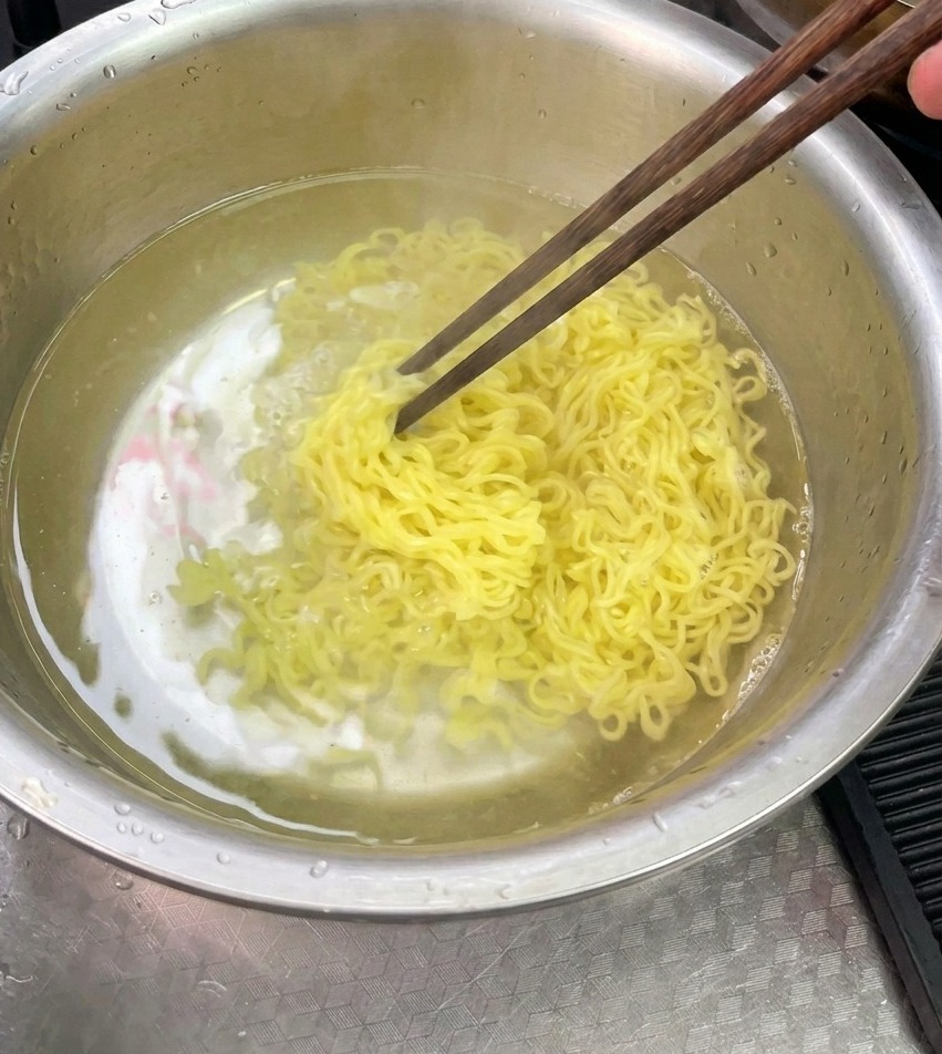 Nouilles jaunes cuites rincées et remuées avec des baguettes dans un bol en acier inoxydable rempli deau froide.