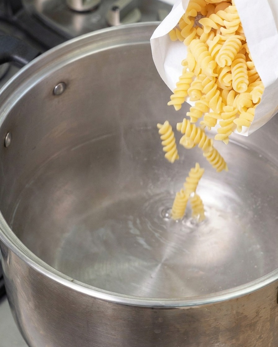 Des fusillis secs versés depuis un sachet blanc dans une grande casserole en inox deau bouillante.