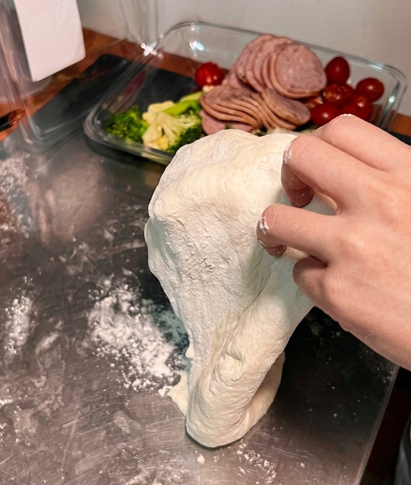 Une pâte à pizza est étirée sur le dos de deux mains pour augmenter son diamètre et sa finesse.