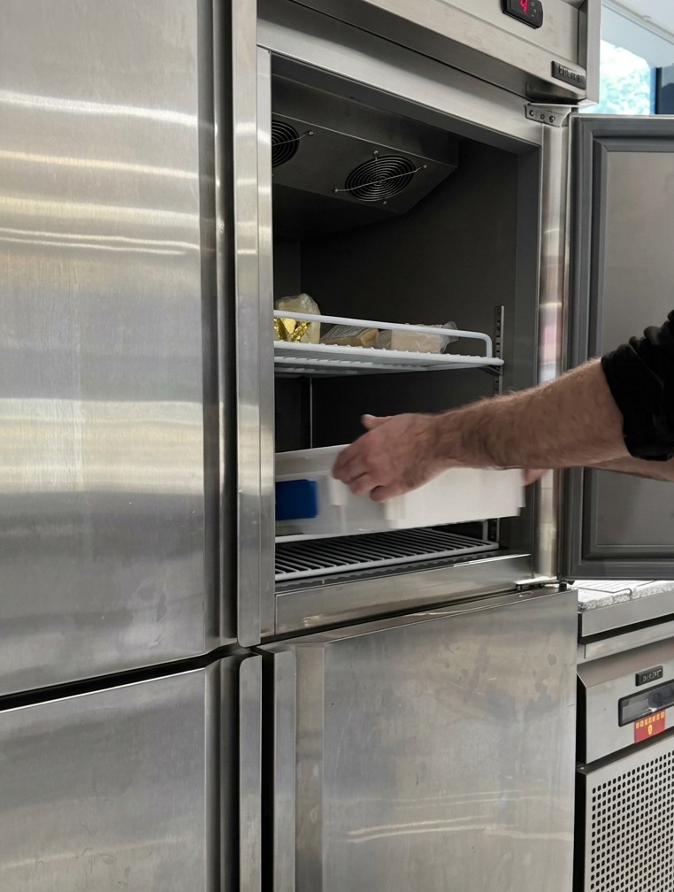 Un bac de pousse blanc rempli de pâtons arrondis glissé sur une étagère à lintérieur dun réfrigérateur professionnel en acier inoxydable.