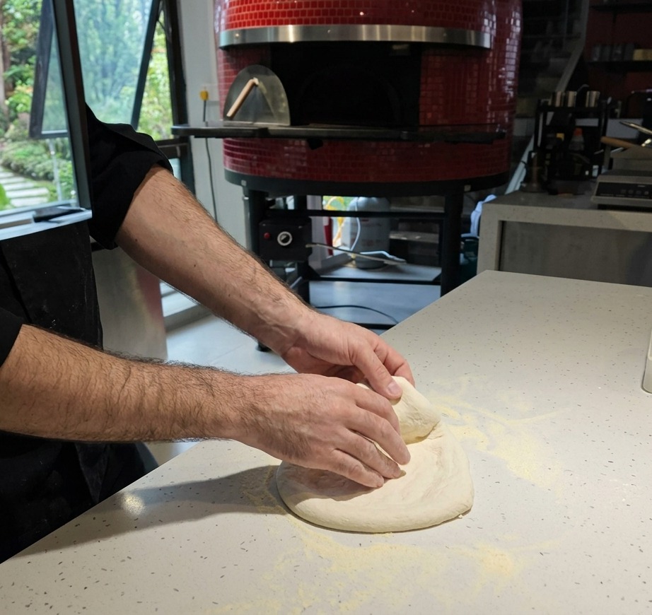 Gros plan sur des mains étirant de la pâte à pizza crue sur un plan de travail blanc couvert de farine.