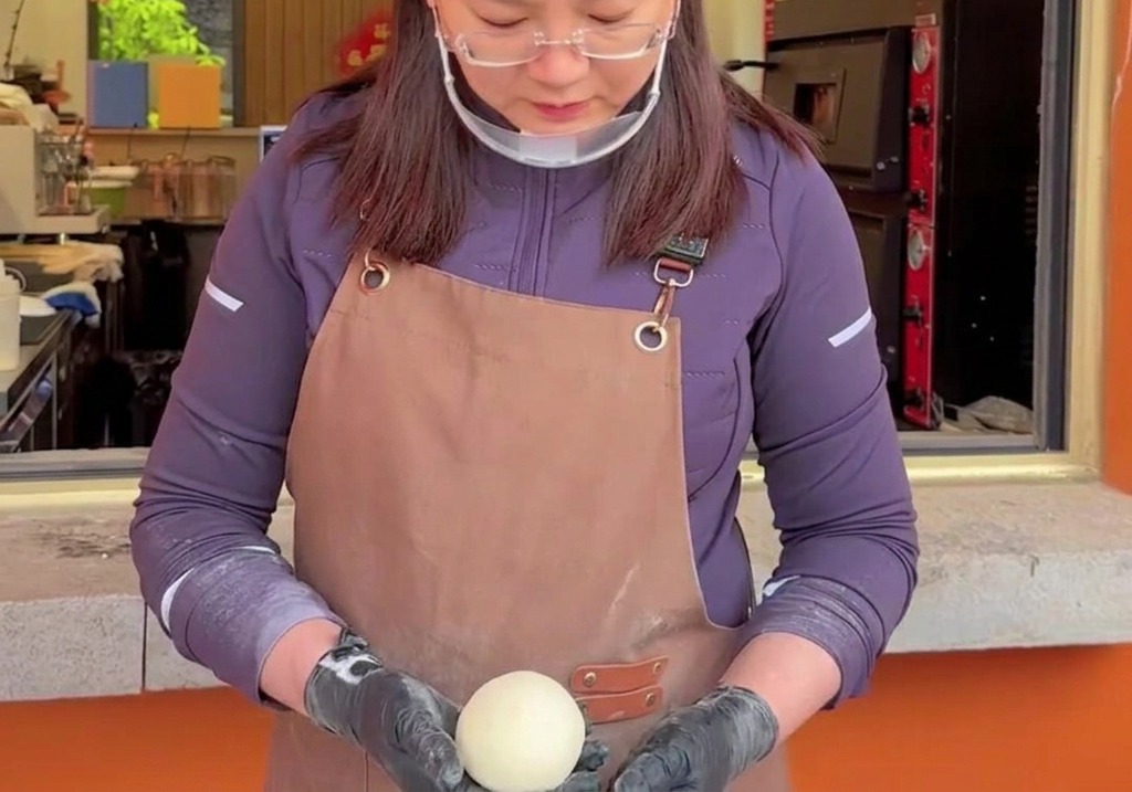 Mains prenant soin de tourner et darrondir une boule de pâte à pizza crue et lisse pour créer une tension superficielle.