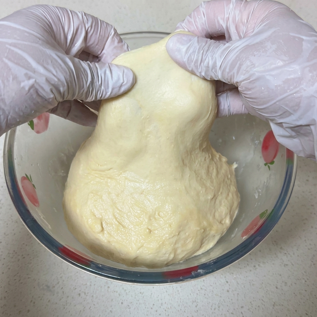 Deux mains étirant délicatement un morceau de pâte à pizza pour former une membrane fine et translucide face à la lumière.