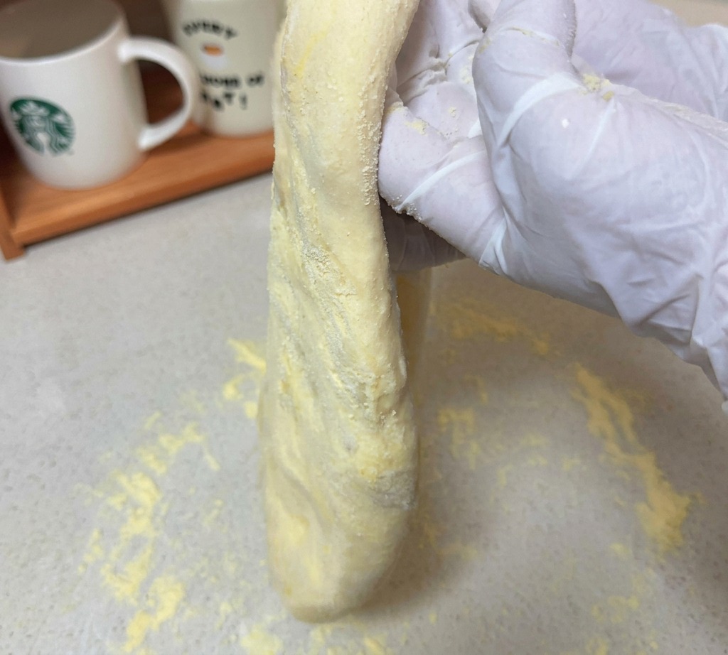 Des mains maintenant verticalement une pâte à pizza bien étirée au-dessus dun plan de travail fariné.