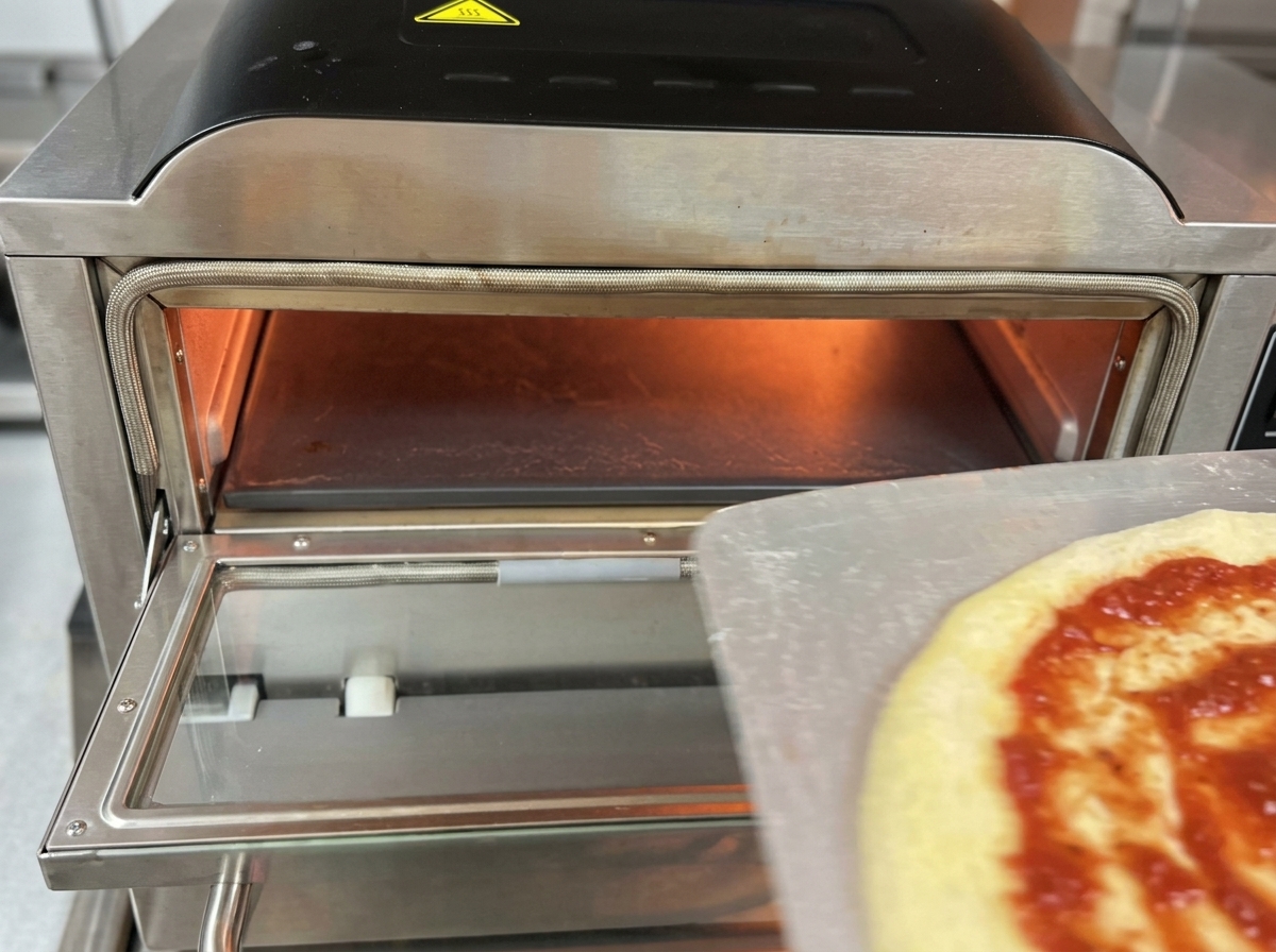 Une pizza crue glissant dune pelle en métal vers lintérieur brûlant dun four à pizza électrique professionnel.