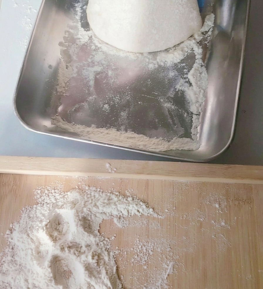 Un pâton de pizza bien rond et souple déposé délicatement sur une planche en bois parsemée de farine.