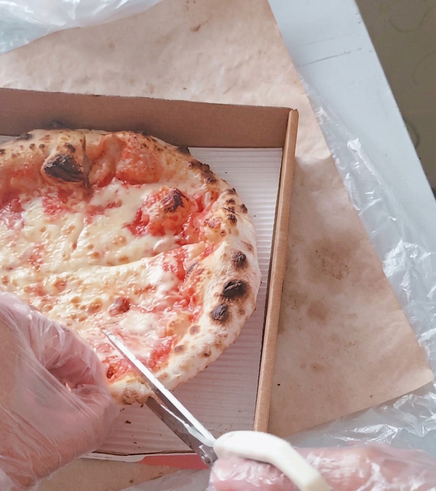 Une personne utilisant des ciseaux de cuisine blancs pour couper une pizza chaude au fromage dans sa boîte en carton.