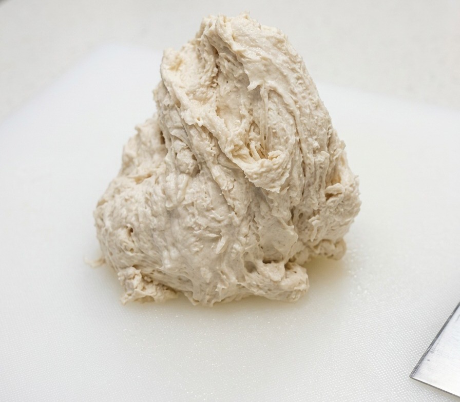 Un pâton humide et rugueux reposant sur une planche à découper en plastique blanc.