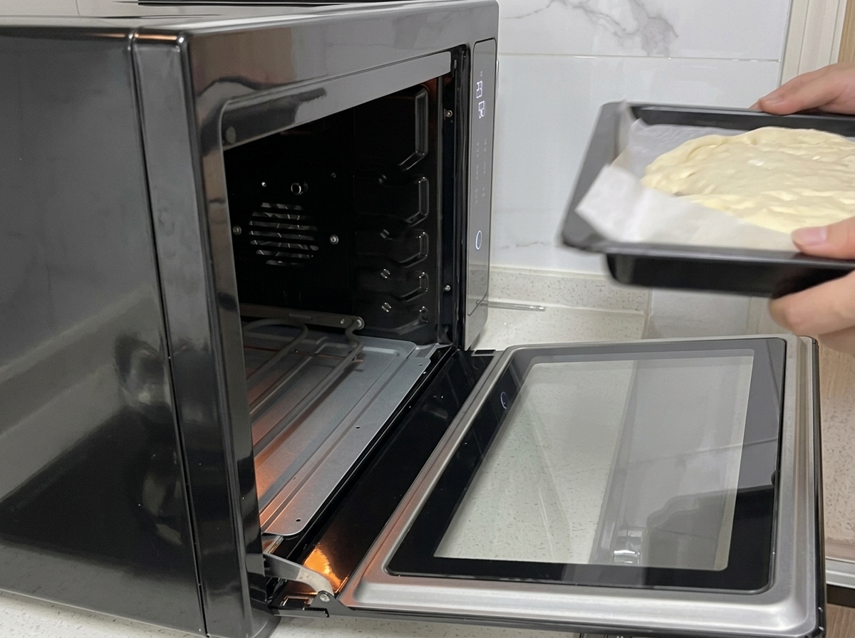Des mains faisant glisser une plaque de cuisson contenant la pâte à pizza dans un four noir ouvert.