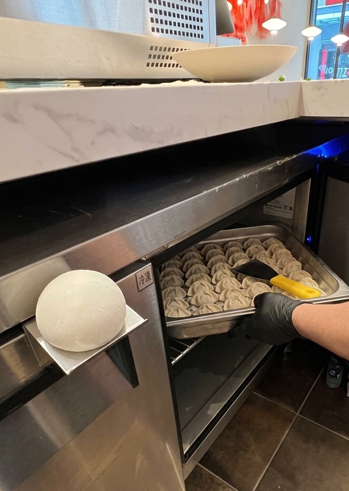 Une main gantée sortant dun meuble réfrigéré professionnel un bac en inox rempli de pâtons ronds et blancs.
