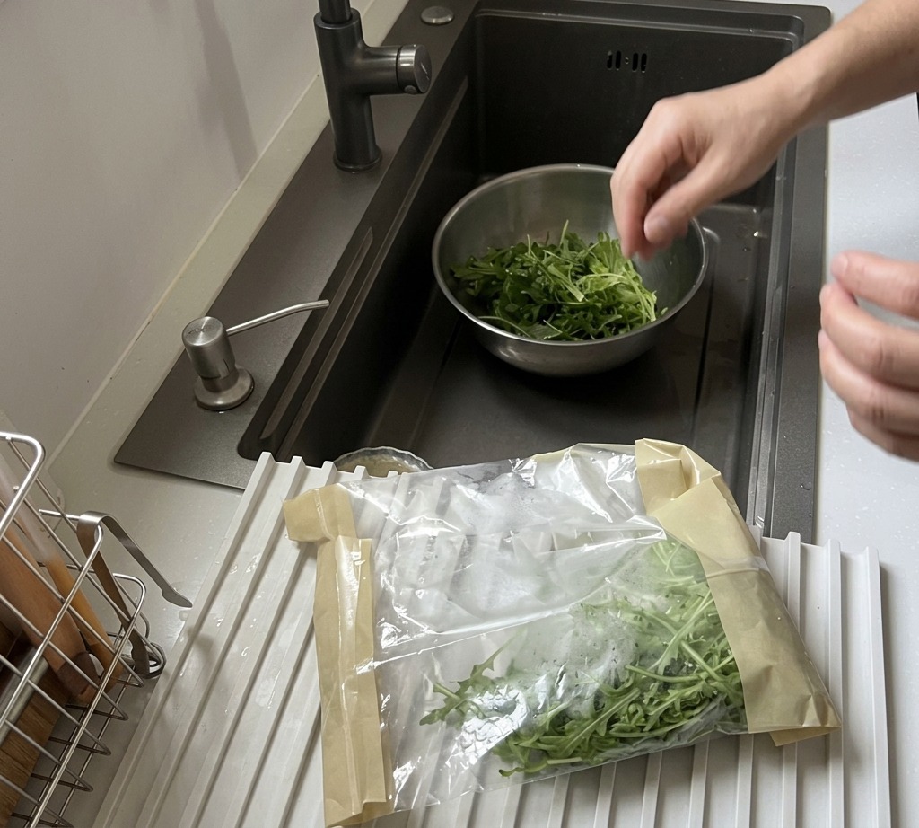 Feuilles de roquette fraîchement lavées dans un bol en acier inoxydable sous le robinet de la cuisine.