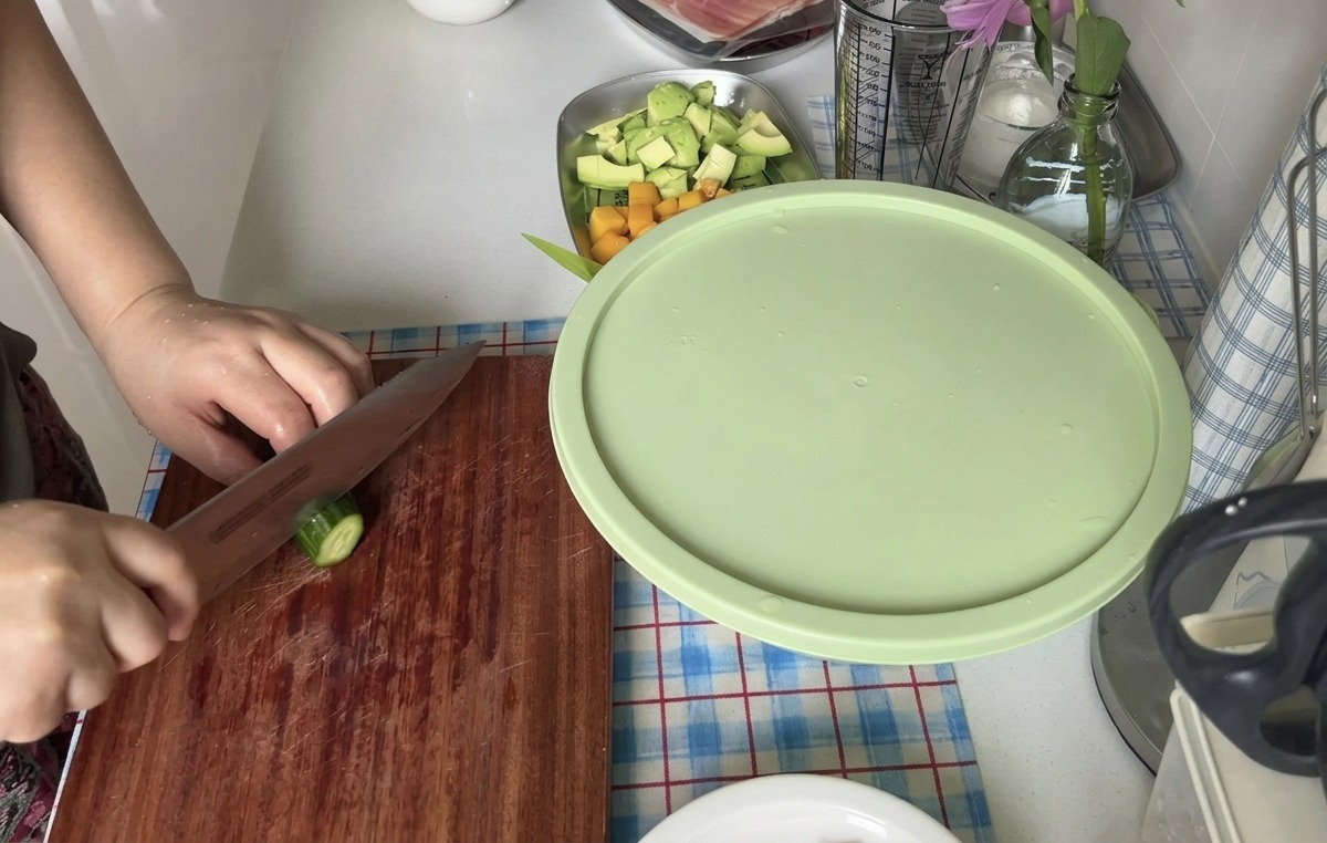 Une personne coupant un concombre frais en fines rondelles à laide dun couteau bien aiguisé sur une planche en bois.