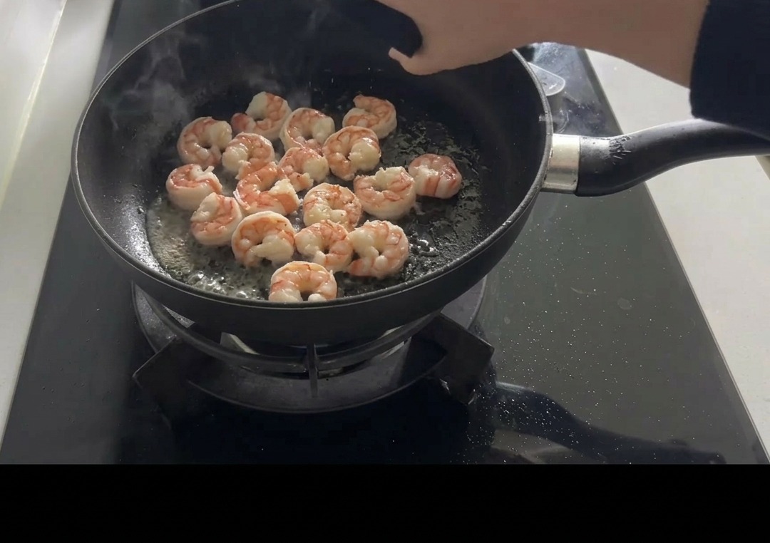 Crevettes roses sautées dans une poêle noire, assaisonnées à la main avec du sel et du poivre.