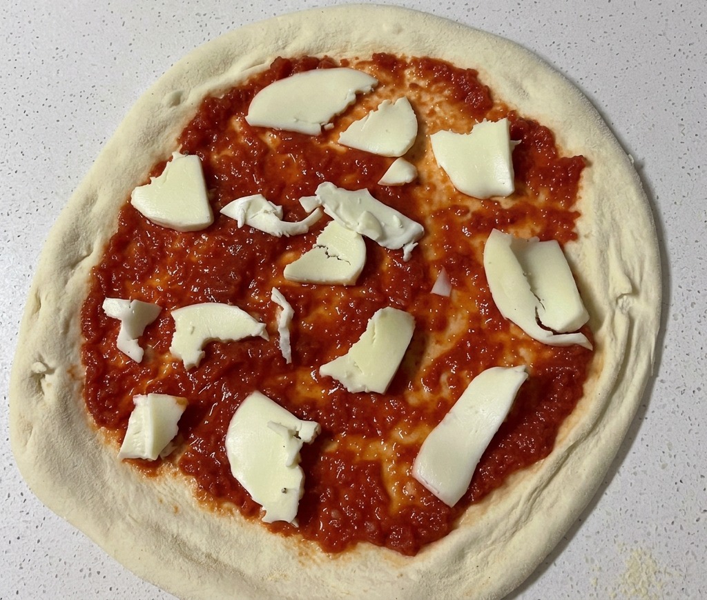 Des morceaux de mozzarella fraîche déchirés à la main déposés sur une base de pizza nappée de sauce tomate.