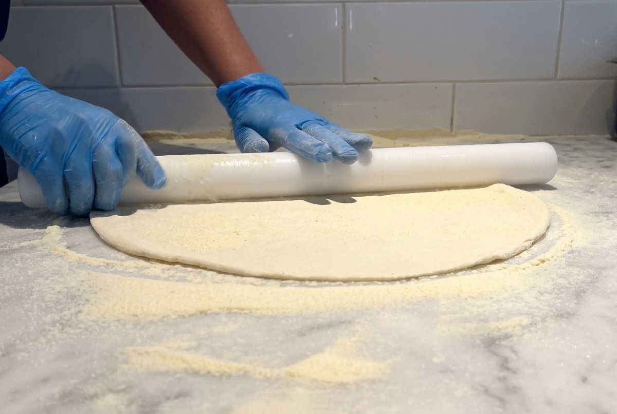 Un rouleau à pâtisserie blanc utilisé pour étaler finement une pâte à pizza sur une table en marbre farinée.