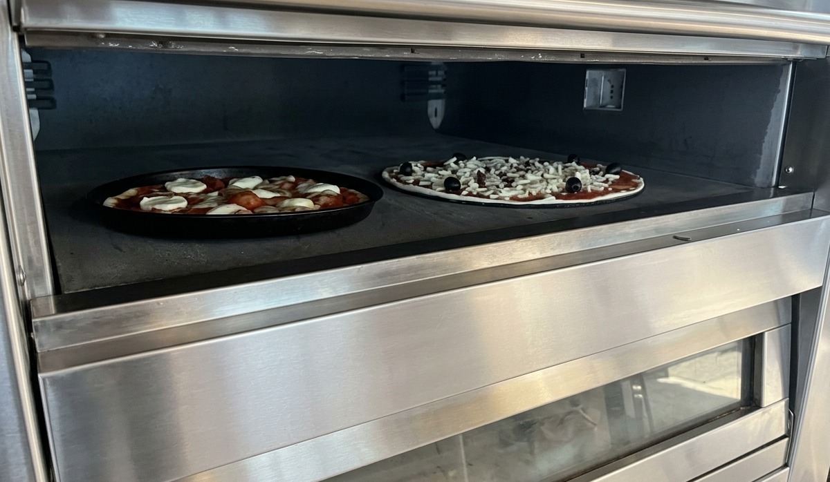 Deux pizzas cuisant sur une pierre à lintérieur dun four professionnel à sole en acier inoxydable.