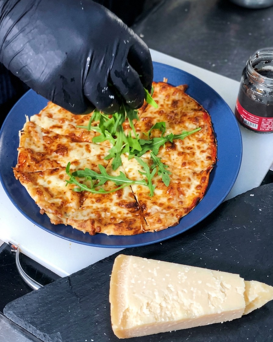 Des feuilles de roquette verte fraîche déposées au centre dune pizza au fromage fraîchement cuite et coupée en parts.