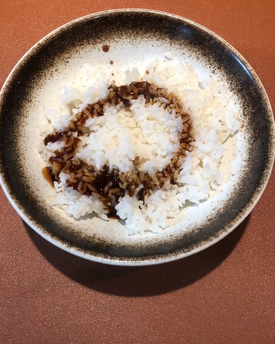 Gros plan sur une sauce sombre et savoureuse aux crevettes versée sur un bol de riz blanc moelleux.
