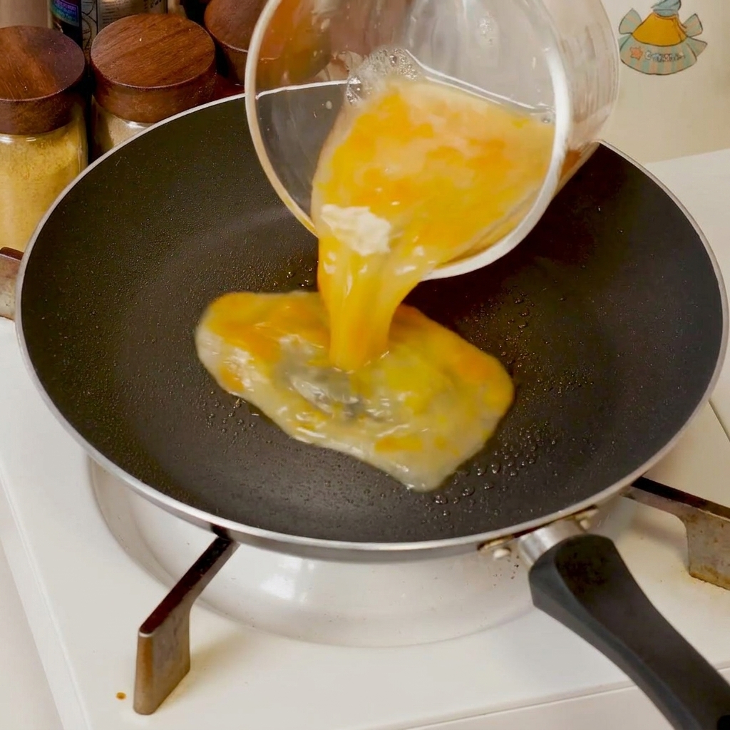 Œufs battus cuisant dans une poêle, poussés vers le centre pour former des curds souples.
