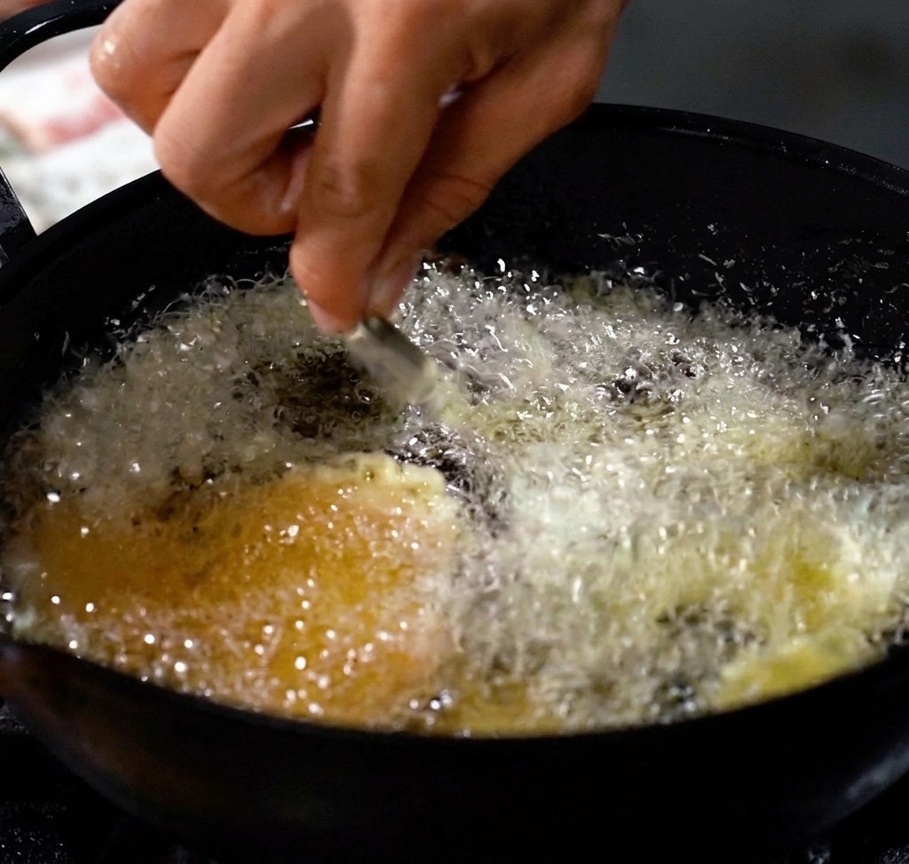 Crevettes en train de frire dans une huile chaude, formant une croûte dorée et croustillante.