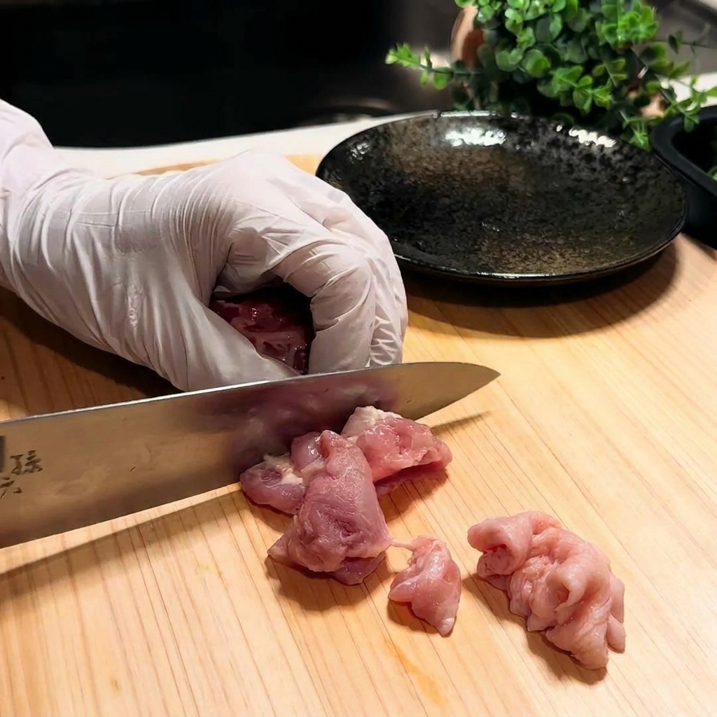 Gros plan sur une cuisse de poulet coupée en petits morceaux sur une planche à découper en bois.