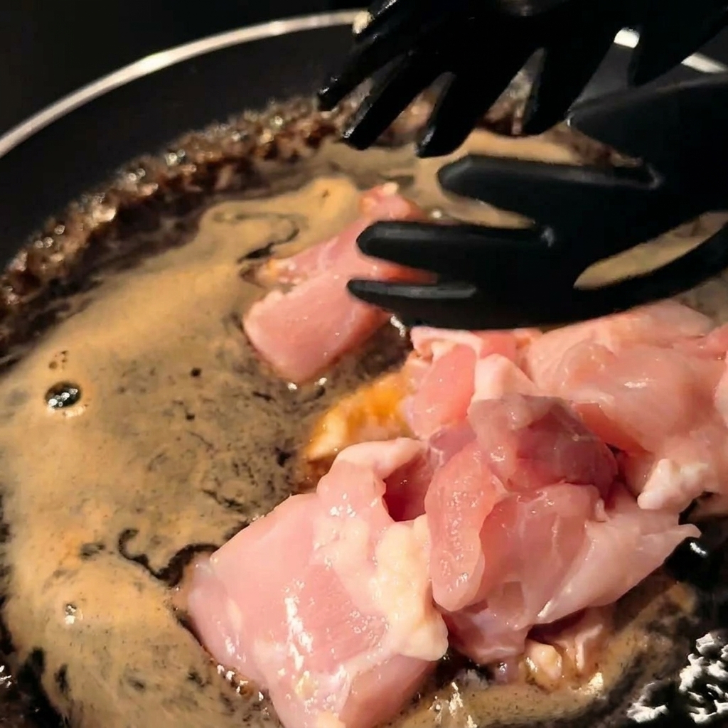 Morceaux de poulet et oignons émincés mélangés à la sauce dans la poêle.