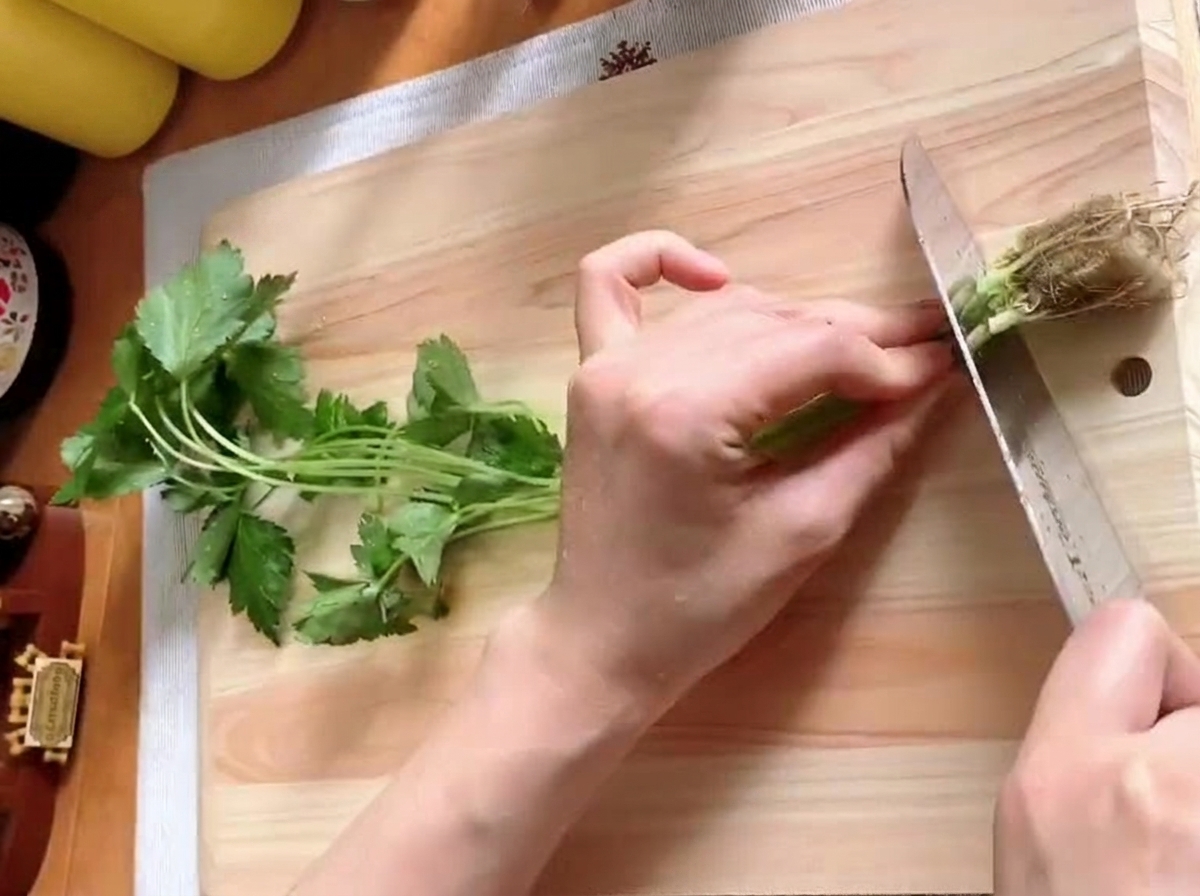 Tiges de mitsuba frais coupées en morceaux sur une planche à découper en bois.
