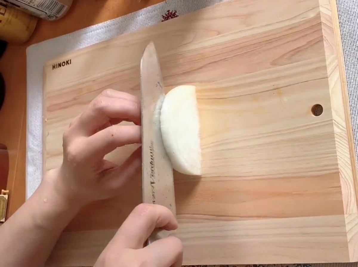 Un demi-oignon finement tranché sur une planche à découper en bois.