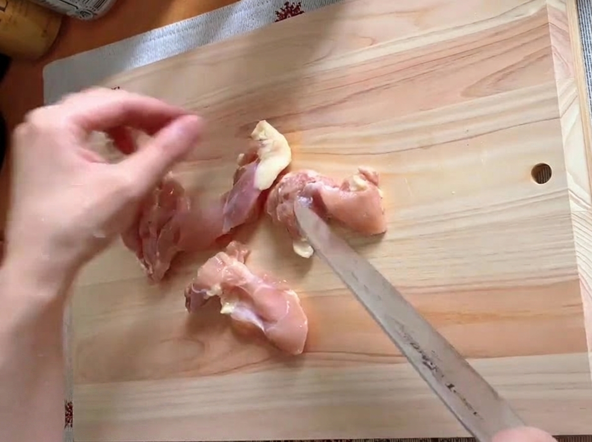 Cuisse de poulet parée et coupée en morceaux sur une planche à découper.