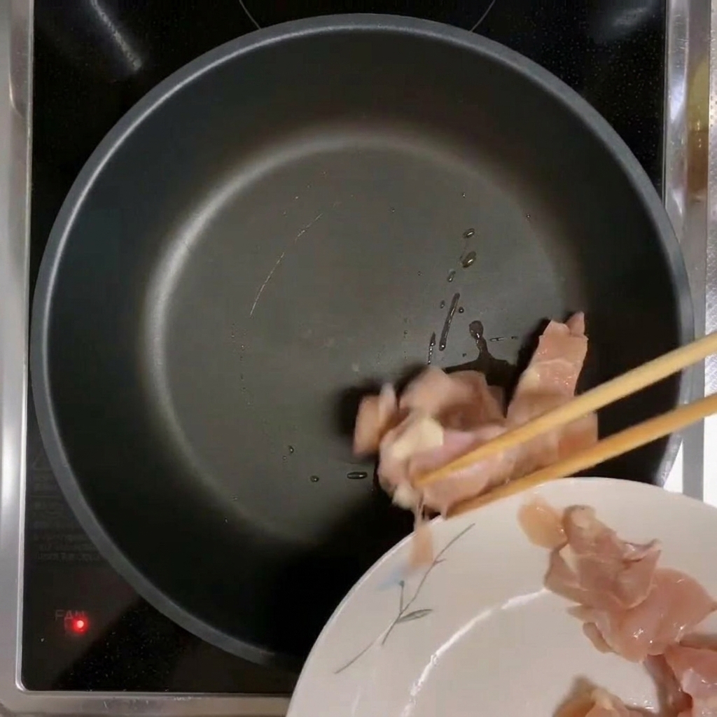 Morceaux de poulet déposés dans une poêle chaude huilée.