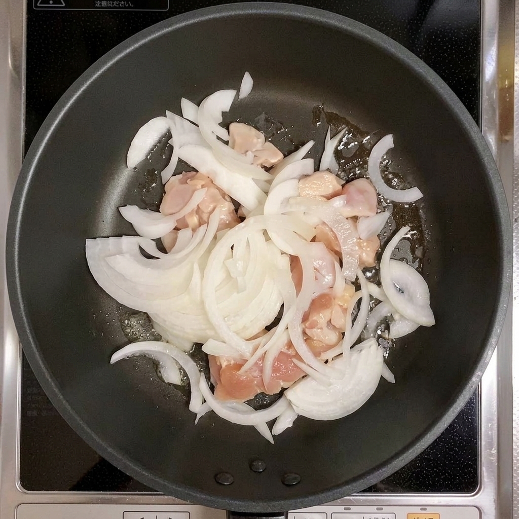Poulet et oignons émincés sautés ensemble dans une poêle.
