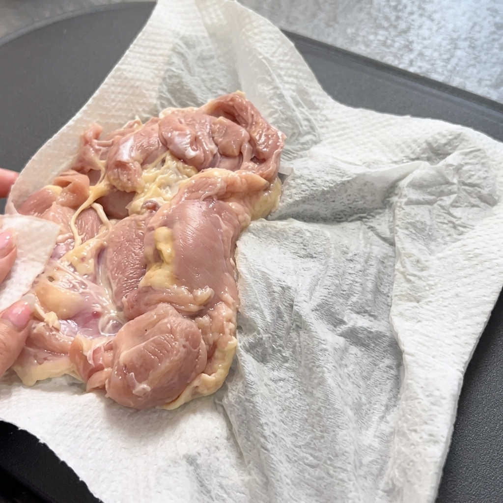 Utilisation dune pince pour déposer délicatement une cuisse de poulet crue dans une poêle chaude.